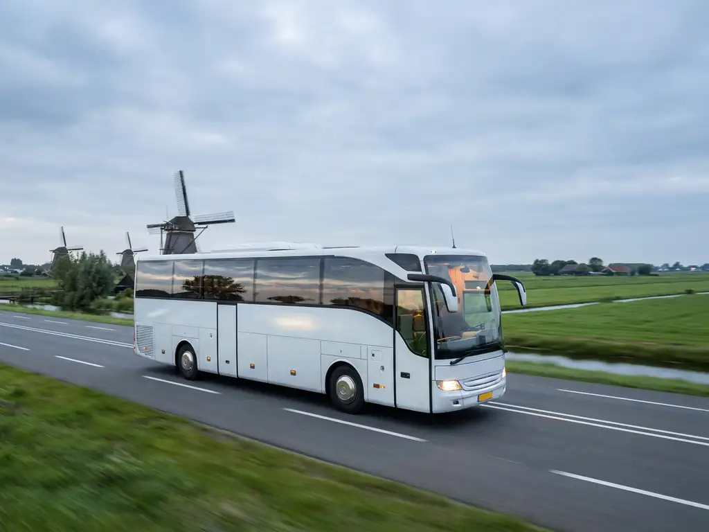 Moderne touringcar rijdt over Nederlandse snelweg langs windmolens en groene polders onder bewolkte lucht.
