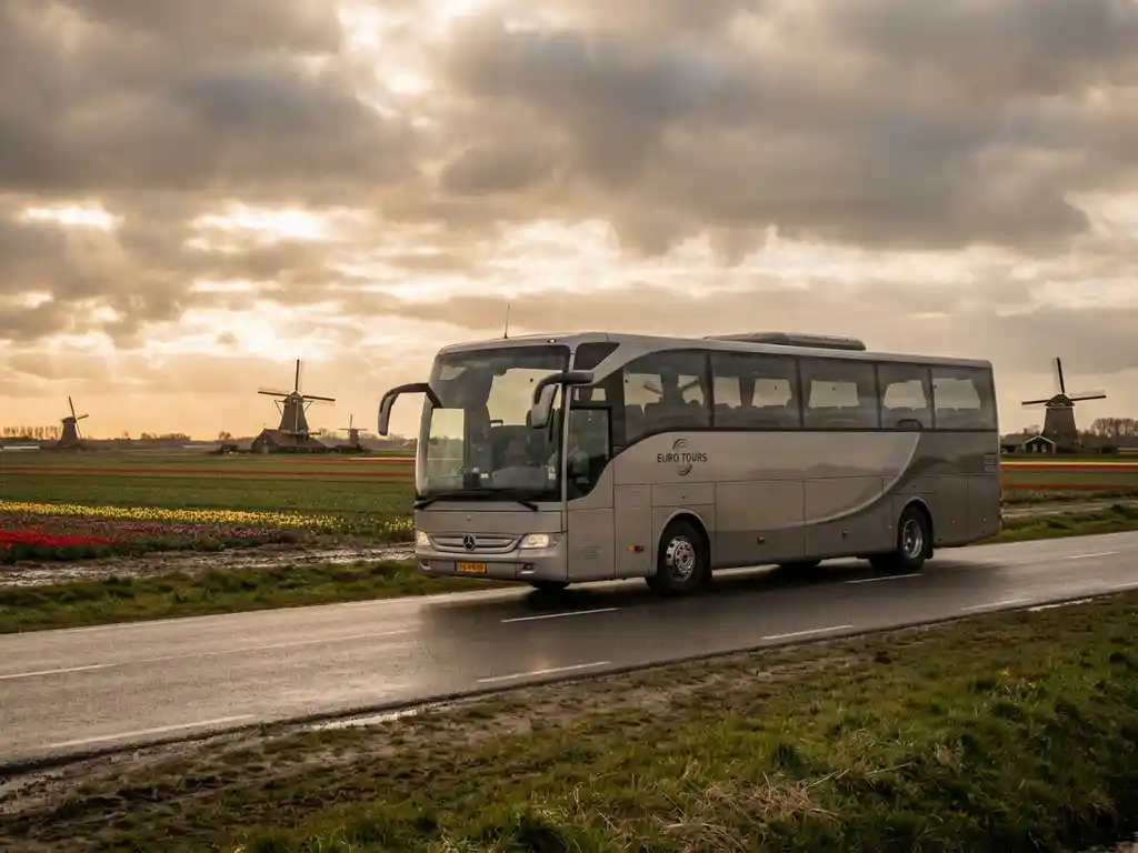 Touringcar rijdt door Nederlands polderland met tulpenvelden en windmolens op de achtergrond onder bewolkte lucht.