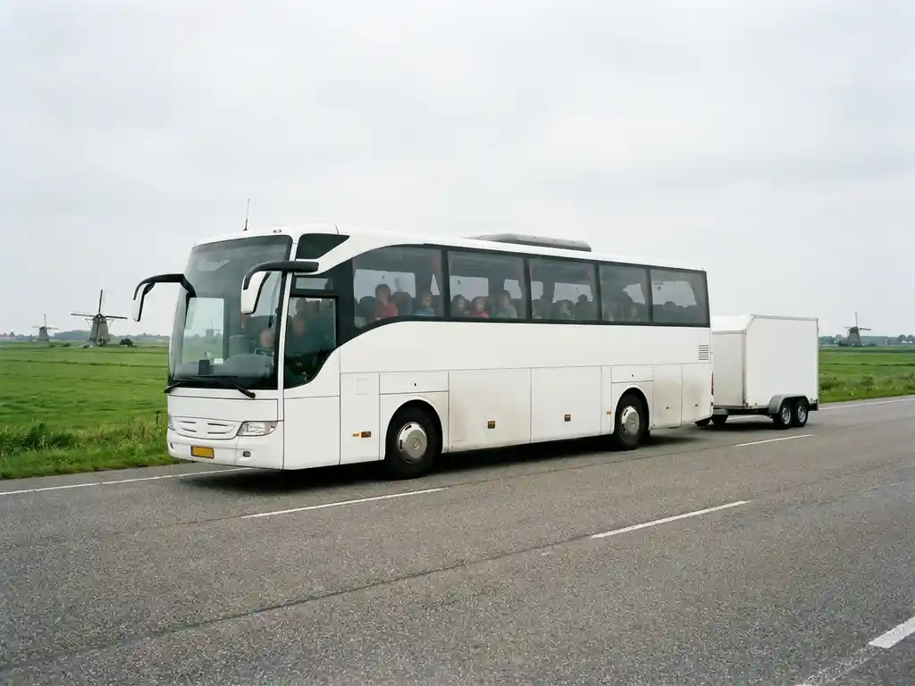 Moderne touringcar met schoolkinderenkoffers op Nederlandse polderweg, groene weilanden en windmolens op achtergrond.