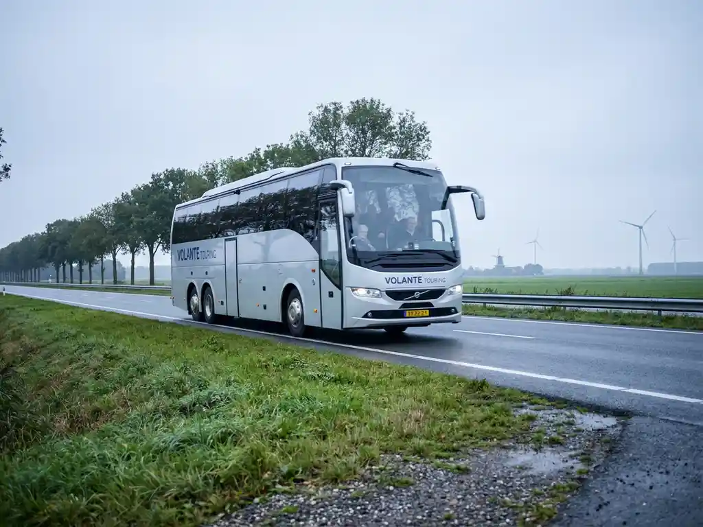 Zilverwitte touringcar met vijftig passagiers op een rechte Nederlandse snelweg, met polders en windmolens op de achtergrond.